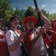 Le journaliste Tristan Lessard-Champagne lors d'un rassemblement d'avant-match de la Coupe du monde de soccer masculin de la FIFA. Il est entour&eacute; de partisans canadiens, souriants, qui brandissent notamment le drapeau du Canada.