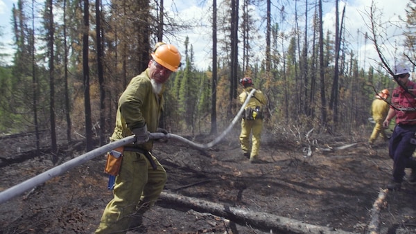 Deux pompiers arrosent un feu de forêt.