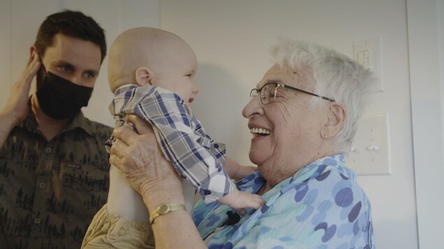 Jacqueline, 91 ans, tiens son arrière-petit-fils dans les bras.